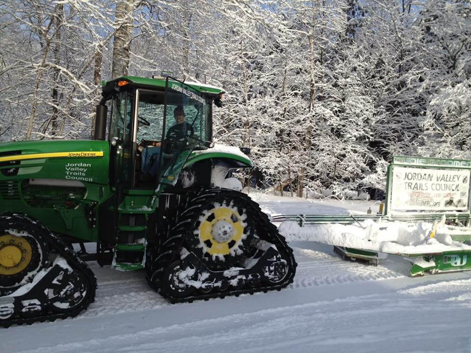 A tractor with tracks in the snow near trees.