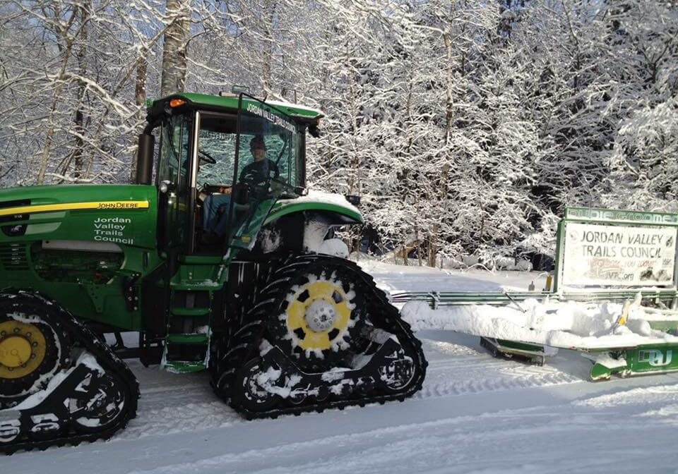 A tractor with tracks in the snow near trees.
